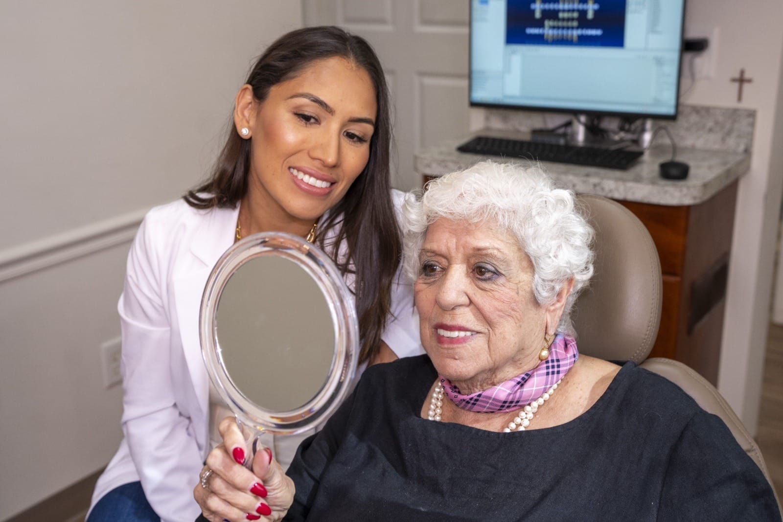 A patient checking her smile after a procedure while Dr. Rodriguez looks on