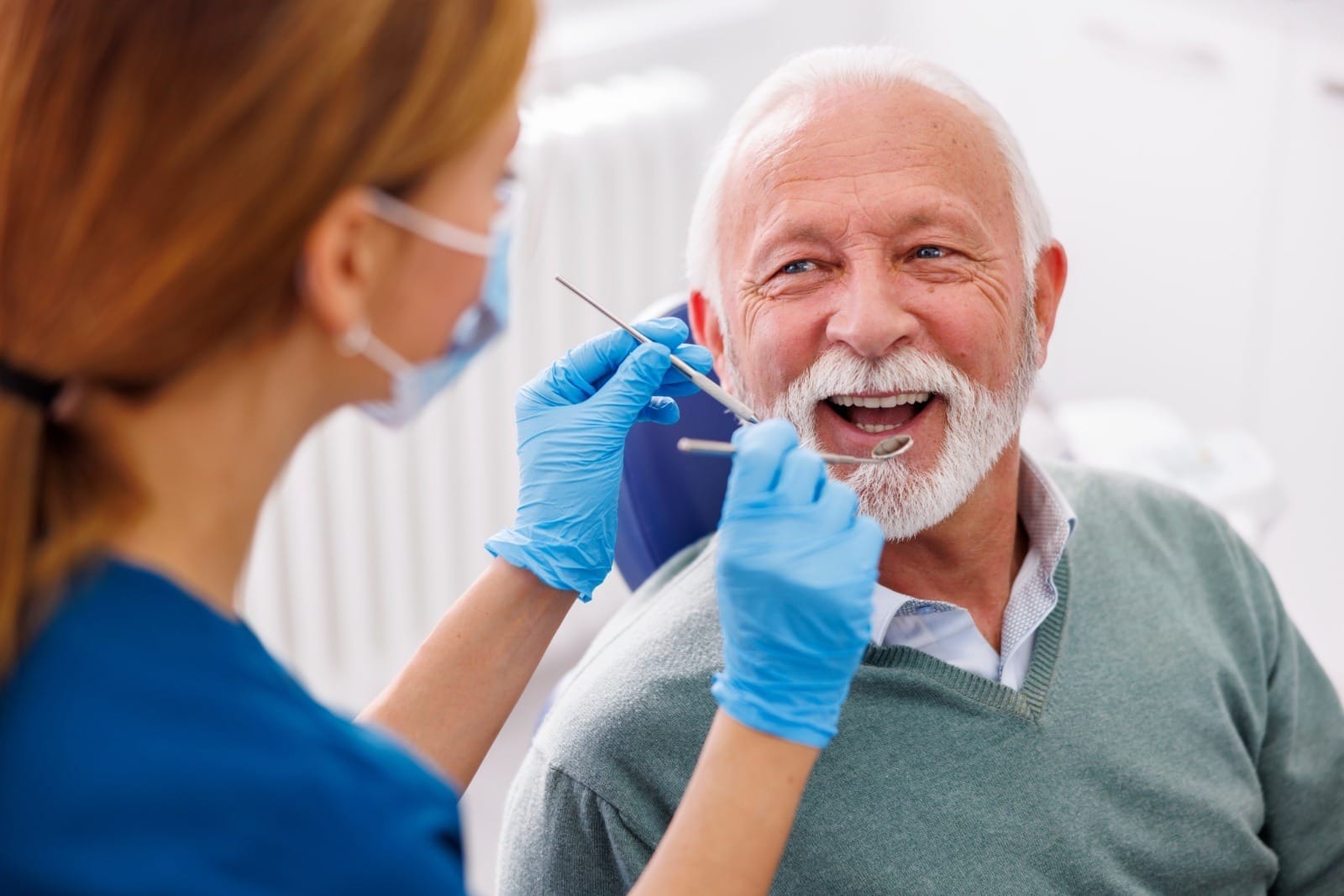 Doctor checking up patient's teeth at dentist office; senior man at dental checkup